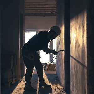 A construction electrician cuts a voltage cable during a repair, silhouette in the light of the setting sun.